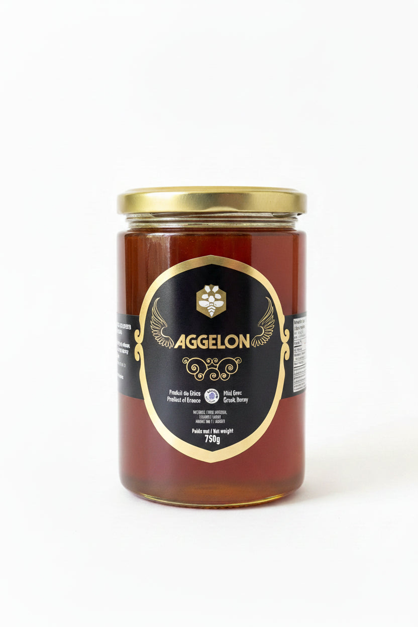 A 750g glass jar of Aggelon Amber Greek Honey, featuring a prominent black and gold label, set on a domestic table with papers in the background.