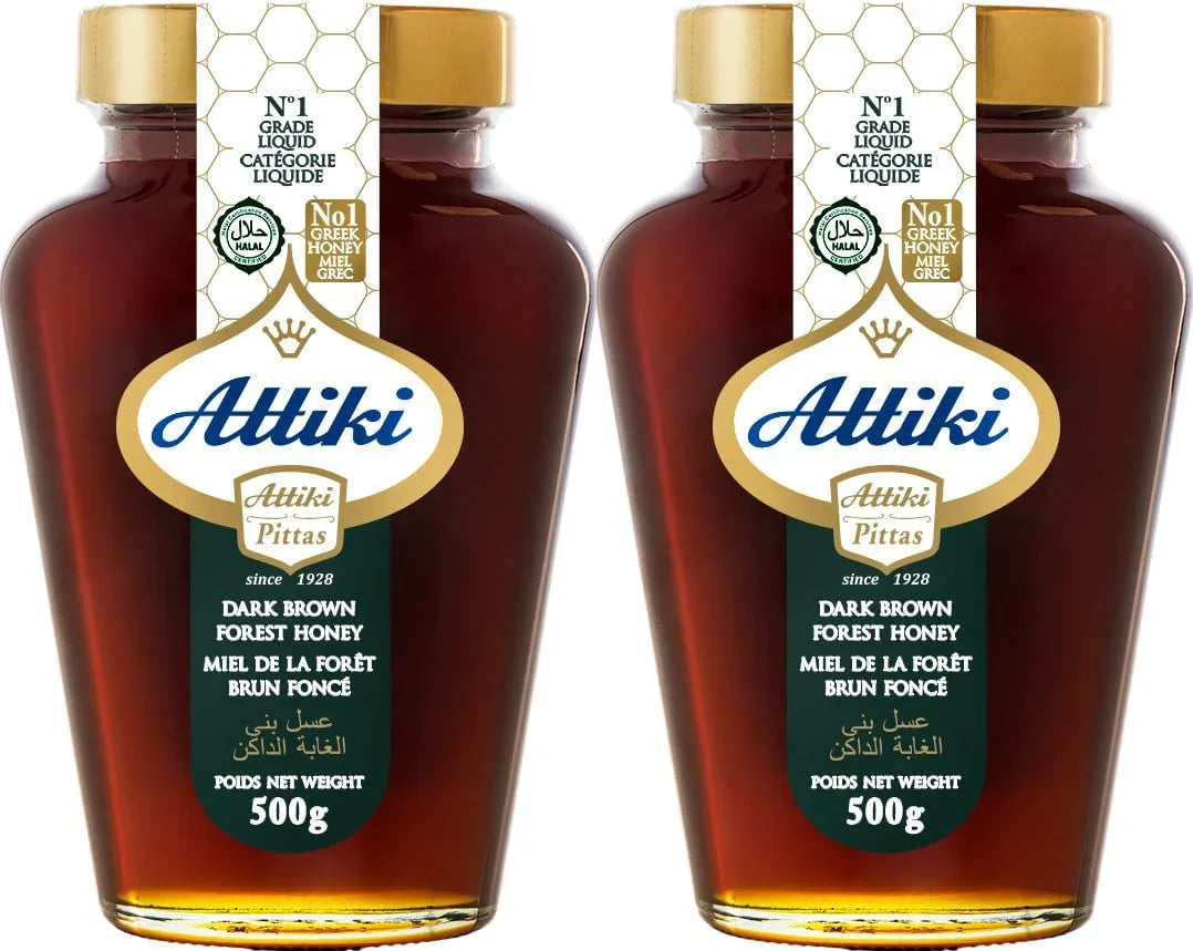 Two bottles of Attiki dark brown forest honey with gold caps on a white background.