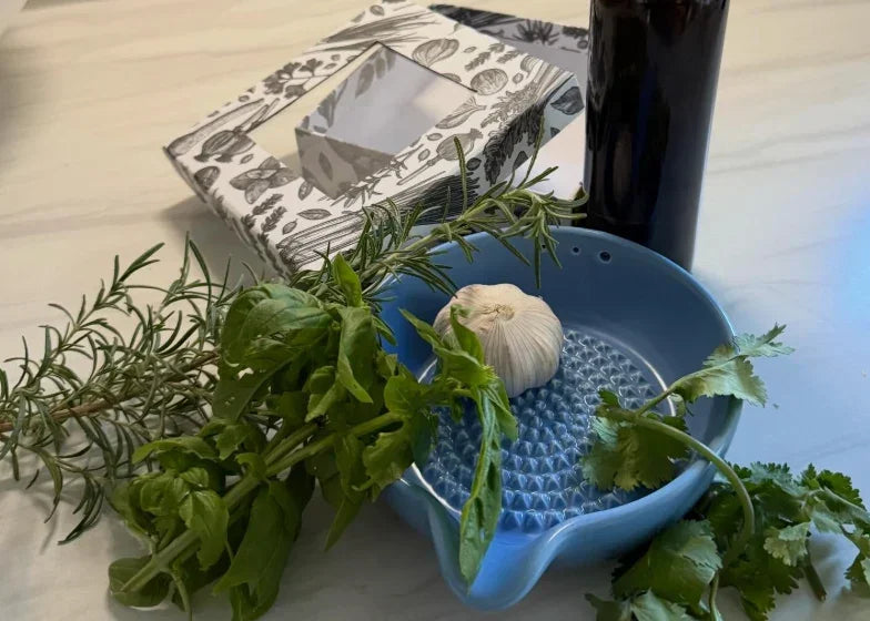 Blue garlic grater bowl with fresh herbs and garlic