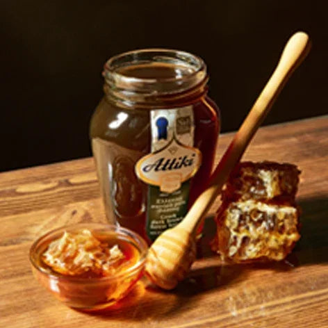 Jar of Attiki honey with a honey dipper and honeycomb on a wooden surface